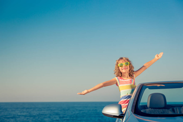 Happy child travel by car. Kid having fun in blue cabriolet. Summer vacation concept - 写真・画像