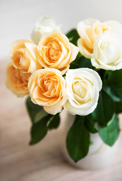 Yellow and white roses in a vase on a table - Фото, изображение