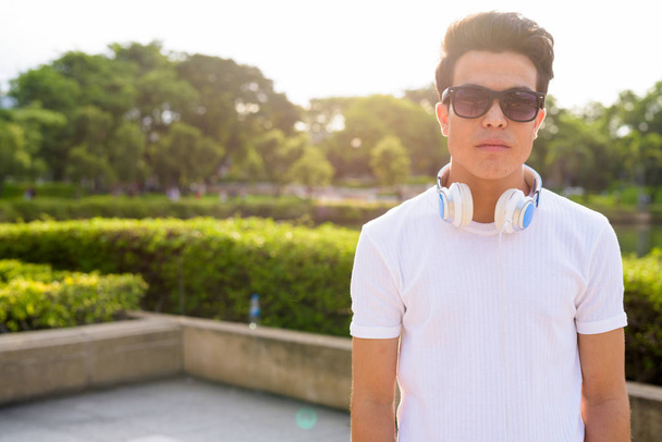 Молодий азіатський чоловік у навушниках під час відпочинку в парку. - Фото, зображення