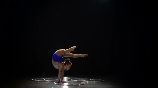 Gymnast stands on the hands performs acrobatic movements. Black background. Slow motion - Video