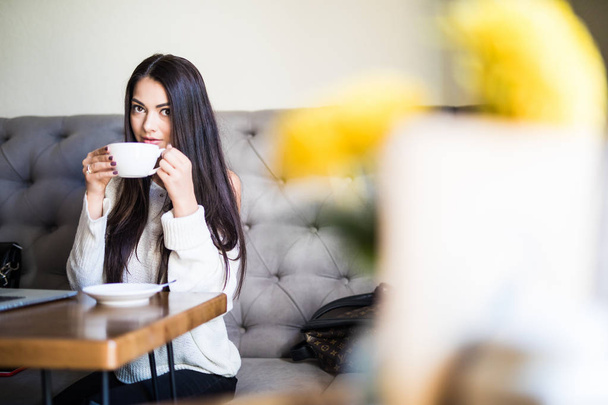 Young woman sitting in coffee shop at wooden table, drinking coffee - Foto, imagen