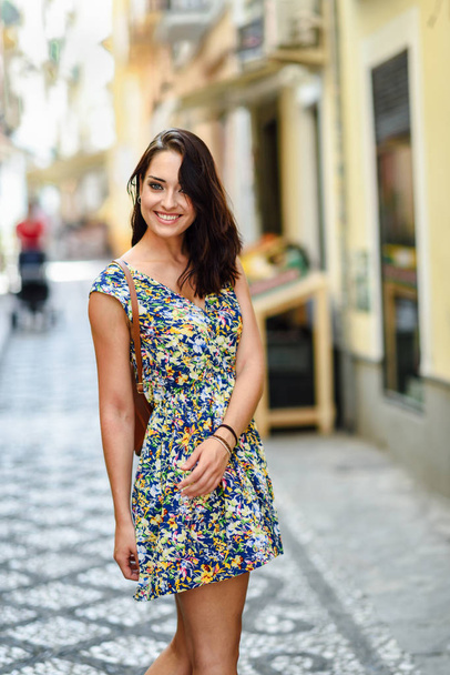 Jeune femme souriante aux yeux bleus avec les cheveux bruns ondulés à l'extérieur. Fille portant une robe de fleur en fond urbain. Concept beauté et mode
. - Photo, image