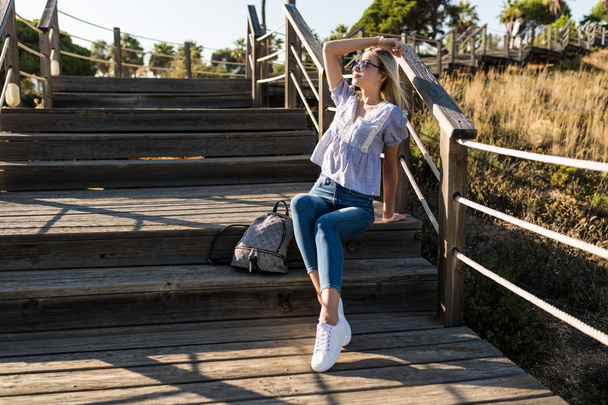 Young woman standing on the wooden stairs that going to the ocean beach - Фото, изображение