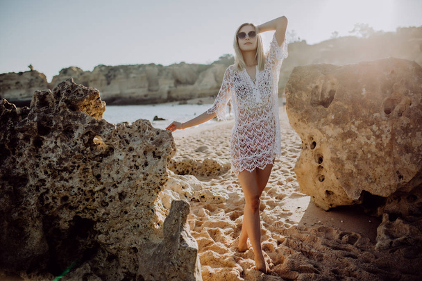 Beautiful young woman tourist walking on beach with rocks on beautiful beach near ocean - Photo, Image