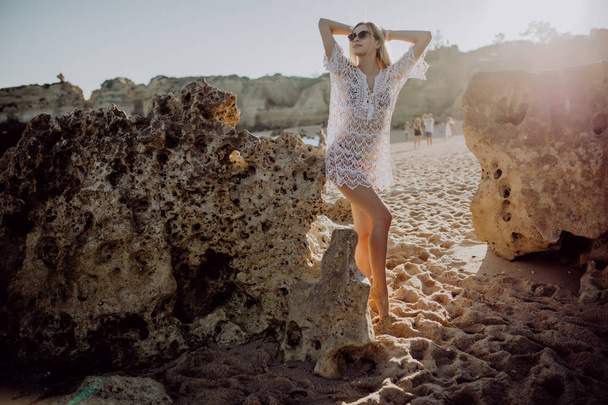 Beautiful young woman tourist walking on beach with rocks on beautiful beach near ocean - Photo, Image