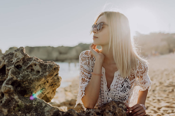 Portré aktív vicces lány az óceán repülő kamera haj és bájos mosollyal beach fehér homokos és sziklák háttérrel - Fotó, kép