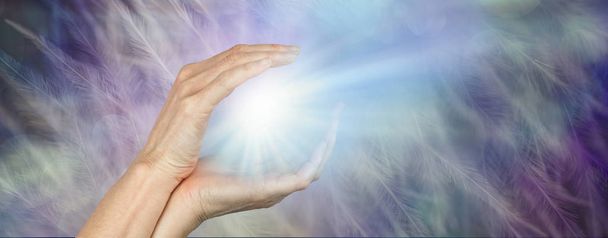 Fenómeno de luz de orbe curativo: las manos femeninas rodearon una brillante ráfaga de luz contra un fondo de plumas con espacio para copiar
  - Foto, imagen