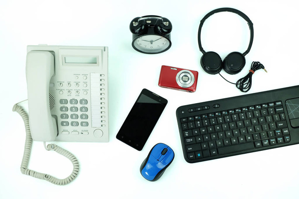 Fehér irodai vezetékes telefon és smartphone, billentyűzet számítógép és asztali óra használt modern elektronikus szerkentyű részére napi használ, elszigetelt fehér background, felülnézet - Fotó, kép