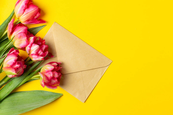 Valentines Womens mothers day concept 8 March Spring, lifestyle blog - pink tulips, craft envelope on yellow background, copy space, top view - 写真・画像