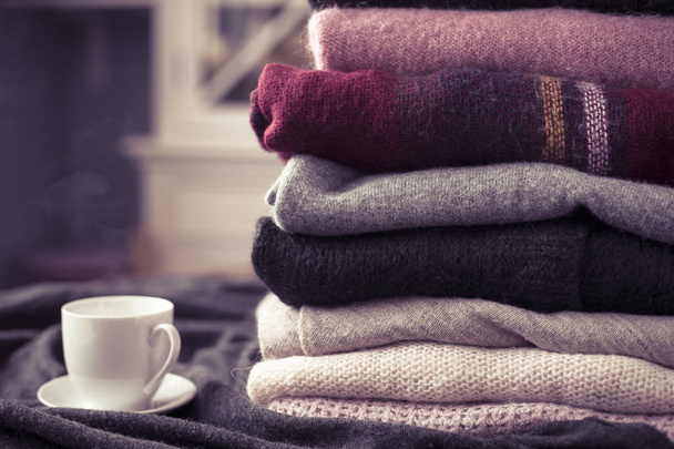 Pile of colorful sweaters with hot drink white cup on the side, background with copy space, cozy hygge wallpaper. Pink filter. - Photo, Image