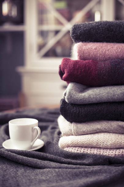 Pile of colorful sweaters with hot drink white cup on the side, background with copy space, cozy hygge wallpaper. Pink filter - Photo, Image
