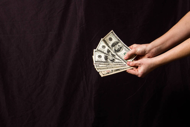 Handen met een fan van dollars op een zwarte achtergrond - Foto, afbeelding