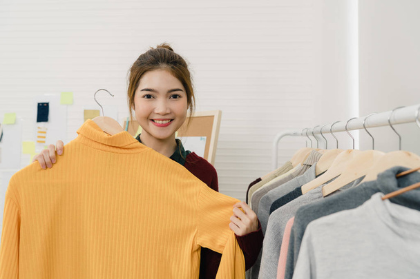 Asian female fashion designer working, checking and choosing clothes design on clothes rack while working in the fashion studio. Lifestyle beautiful professional designer women working concept. - Zdjęcie, obraz