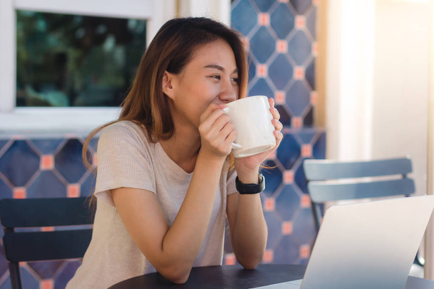 Азиатские молодые женщины в умной повседневной одежде, работающие, посылая электронную почту на ноутбук и выпивая кофе, сидя в кафе. Общение женщин в стиле жизни и работа в концепции кафе
. - Фото, изображение