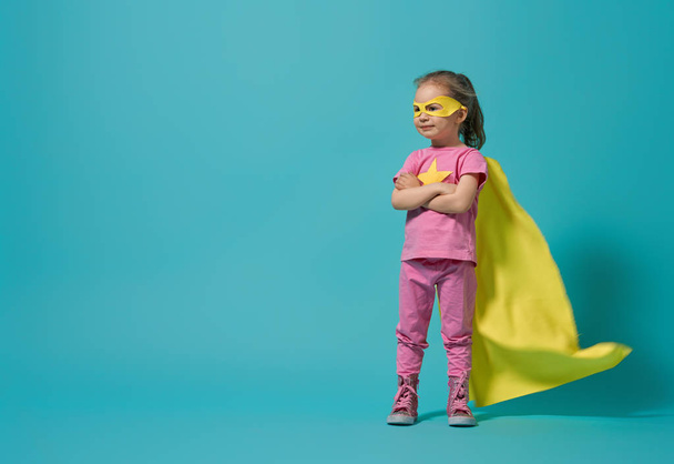 Little child playing superhero. Kid on the background of bright blue wall. Girl power concept. Yellow, pink and  turquoise colors. - 写真・画像