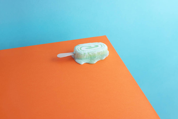 Melting ice cream popsicle over orange and blue background - Fotó, kép