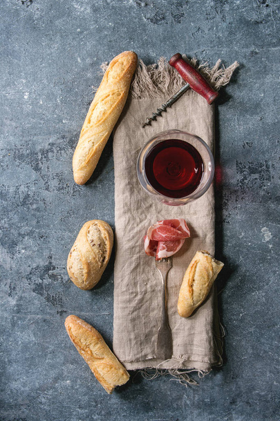 Antipasto meat sliced jamon on fork with artisan bread variety and glass of red wine on cloth over blue texture background. Flat lay, space. Appetizer concept - Fotografie, Obrázek