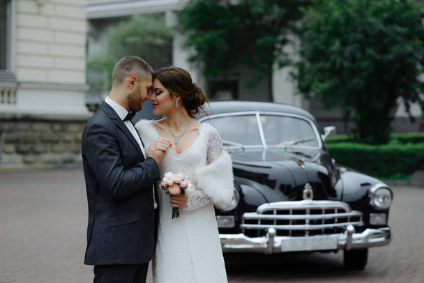 glückliches Luxus-Hochzeitspaar küsst und umarmt sich im Herbst im Retro-Look mit Bouquet-Auto - Foto, Bild
