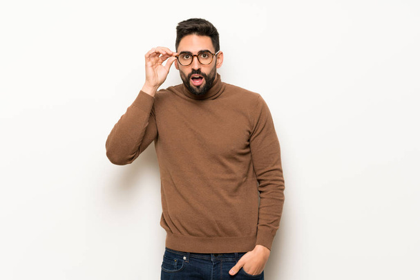 Handsome man over white wall with glasses and surprised - Zdjęcie, obraz