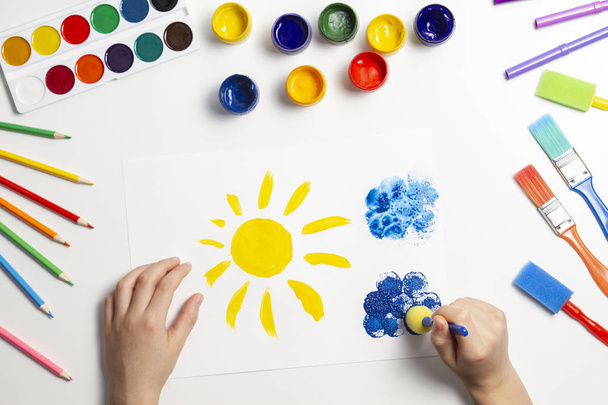 Kid hands painting at the table with art supplies, top view - 写真・画像
