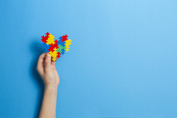 Child hand holding colorful heart on blue background. World autism awareness day concept - Valokuva, kuva