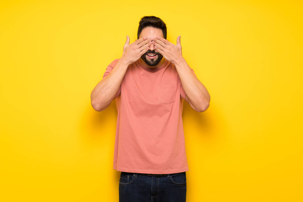 Handsome man over yellow wall covering eyes by hands. Surprised to see what is ahead - Photo, Image