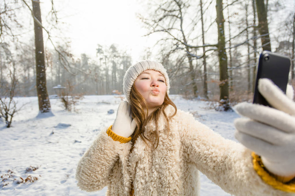 beautiful happy young woman taking selfie with smartphone in winter park   - Foto, Bild
