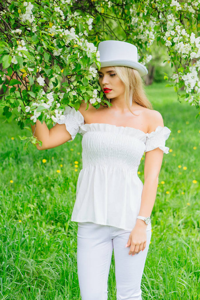 Sexy modern bride in white cylinder hat enjoing bloomin apple tree flowers - Foto, immagini