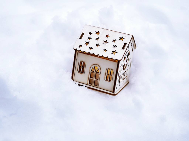  ein kleines Spielzeugdekorationshaus mit beleuchteter Beleuchtung im Schnee, das Konzept der Winterferien, Weihnachten, ein neues Haus im neuen Jahr, Wohnkomfort - Foto, Bild