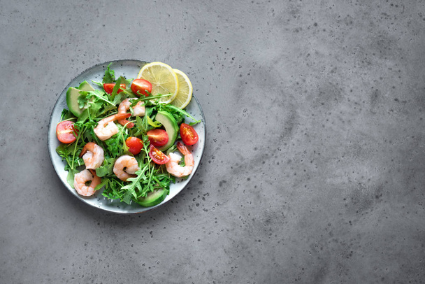 Avocado Shrimp Salad with Arugula and Tomatoes on grey stone background, copy space. Healthy diet green salad with Shrimps (prawns), avocado, cherry tomato and arugula. - Foto, Imagem