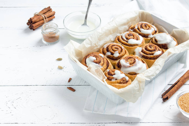 Cinnamon rolls or cinnabon, homemade recipe of sweet traditional dessert buns with white cream sauce on white wooden background. - Foto, immagini