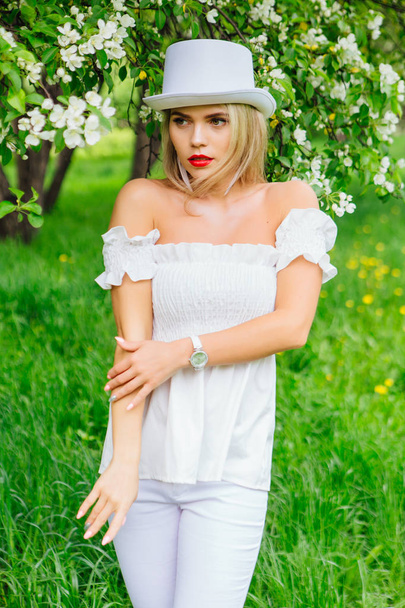 Sexy modern bride in white cylinder hat enjoing bloomin apple tree flowers - Фото, изображение
