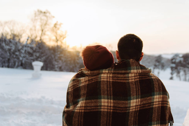 Egy fiatal férfi és a nő ül össze, és nézi a téli naplementét. - Fotó, kép