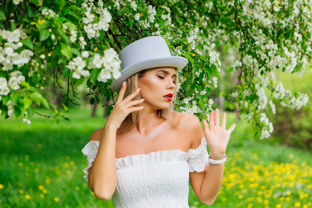 Sexy modern bride in white cylinder hat enjoing bloomin apple tree flowers - Photo, image