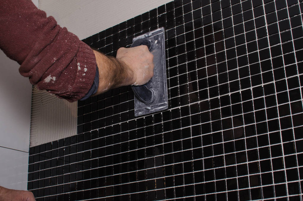 Koti korjaus: asentamalla mosaiikki laatta seinälle. Työntekijä peittää seinän liimalla hammaslastalla
. - Valokuva, kuva