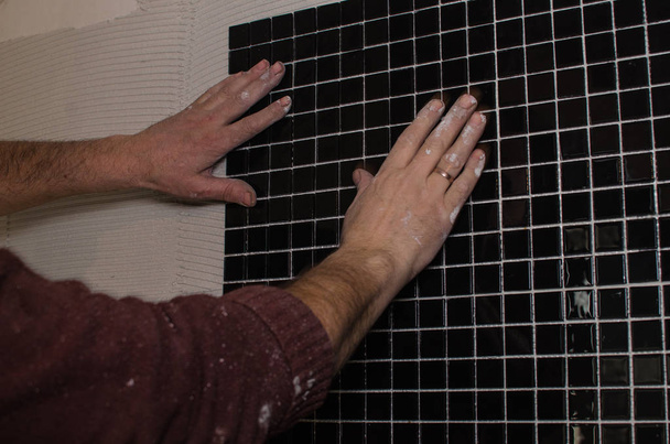Reparatur zu Hause: Installation der Mosaikfliese an der Wand. ein Arbeiter verklebt die Wand mit einem gekerbten Spachtel. - Foto, Bild