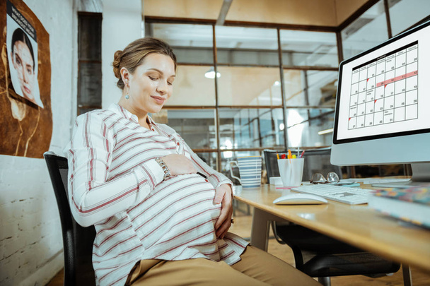 Femme enceinte assise après le travail au bureau et touchant son ventre
 - Photo, image