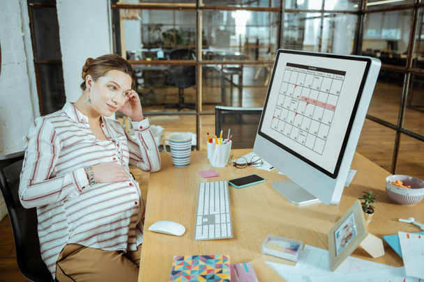 Pregnant dark-haired woman feeling a little bit busy after work - 写真・画像