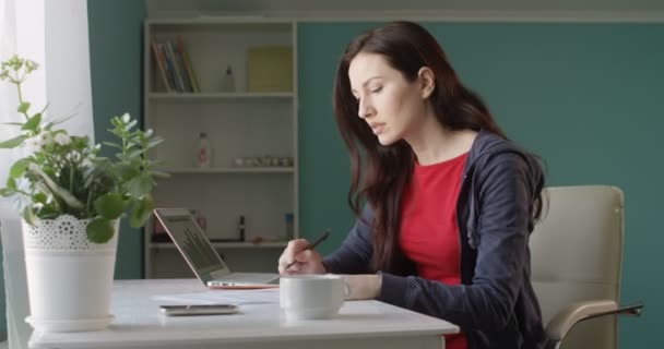 Upset Brunette Small Business Owner Stressed over Bad Sales Sitting at the Home Office Desk Working on Notebook and Throwing Papers - Imágenes, Vídeo