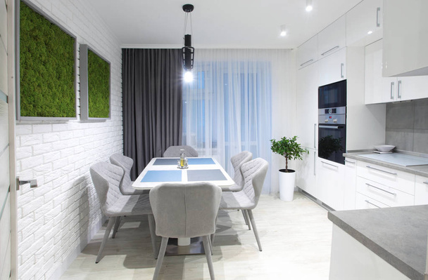 White kitchen interior with grey chairs,moss on the wall in new luxury home with lights on. - Foto, imagen