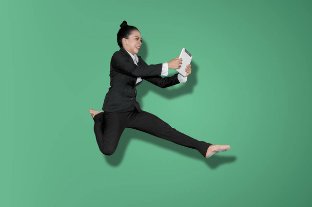Asian businesswoman using a digital tablet while leaping in the studio with green screen - Foto, Imagem