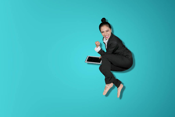 glückliche Geschäftsfrau feiert Erfolg, indem sie im Studio springt und ein digitales Tablet in der Hand hält - Foto, Bild