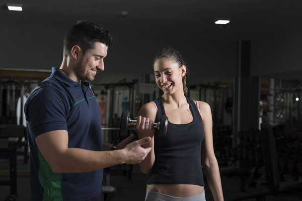 Man helping woman training biceps at gym - Foto, Imagen