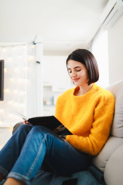 Woman reading book at home sitting on comfortable sofa at a rest day - Photo, image