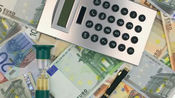 Rotation of the hourglass and calculator, pen lying on the euros. Top view. - Video