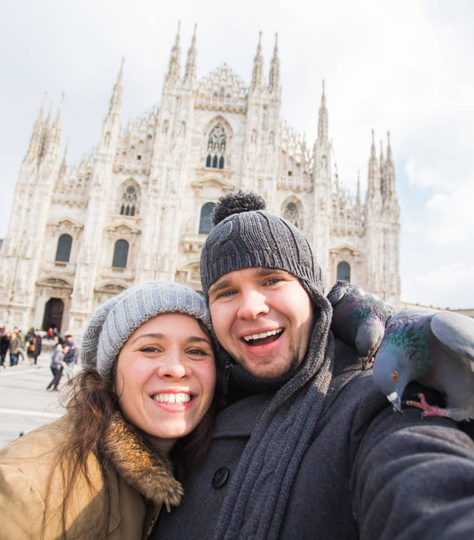 Χειμώνας ταξίδια και διακοπές έννοια - χαρούμενων τουριστών λήψη αυτοπροσωπογραφία με αστεία περιστέρια μπροστά στον καθεδρικό ναό Duomo στο Μιλάνο - Φωτογραφία, εικόνα