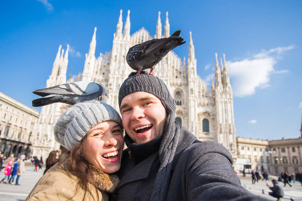 Winter travel and vacations concept - Happy tourists taking a self portrait with funny pigeons in front of Duomo cathedral in Milan - Photo, Image