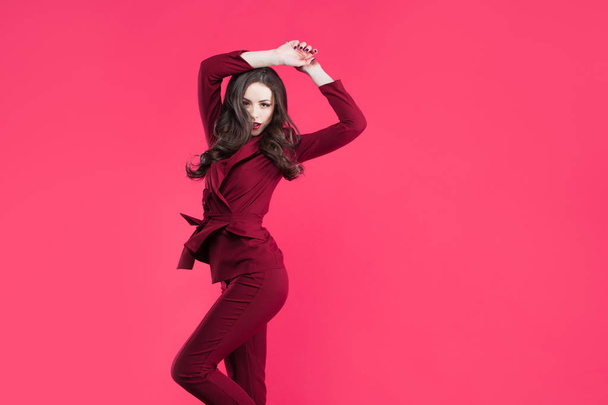 Jumping glamorous girl. Attractive young brunette dressed in Burgundy color, pink color background - Photo, Image