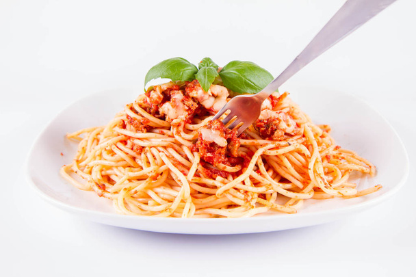Spaghetti bolognese eaten with a fork decorated with basil on a white background - Fotografie, Obrázek