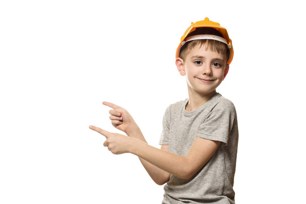 Chlapec v oranžové stavbařskou přílbu ukazuje ukazováčky stranou. Portrét. Izolovat na bílém pozadí - Fotografie, Obrázek
